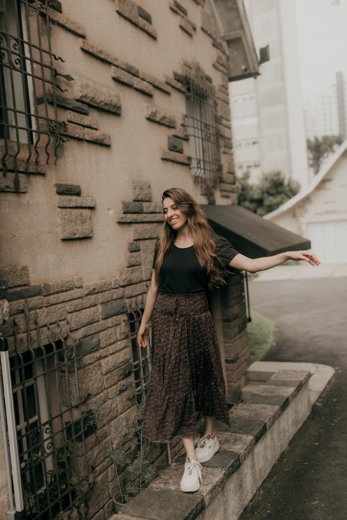 Woman smiling in chic attire near vintage stone architecture outdoors.
